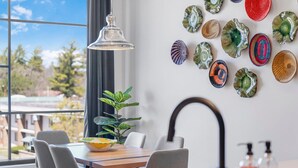 Et spiseområde med et bord, stole, en hængende lampe, en potteplante og en væg med dekorative tallerkener.