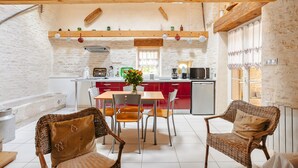 A cozy kitchen with a dining area, featuring a wooden ceiling, white brick walls, and a central island with a sink and stove. - Gîte L'Etable - Les Gites Du Moulin: private terrace, garden, Wi-Fi in Saint-Hilaire-la-Palud (Saint-Hilaire-la-Palud)