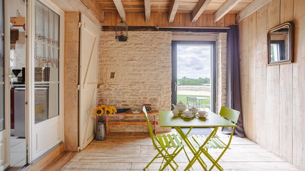 A rustic room with a stone wall, wooden ceiling, a table with chairs, a window with a view, and a door. - Gîte L'Etable - Les Gites Du Moulin: private terrace, garden, Wi-Fi in Saint-Hilaire-la-Palud (Saint-Hilaire-la-Palud)