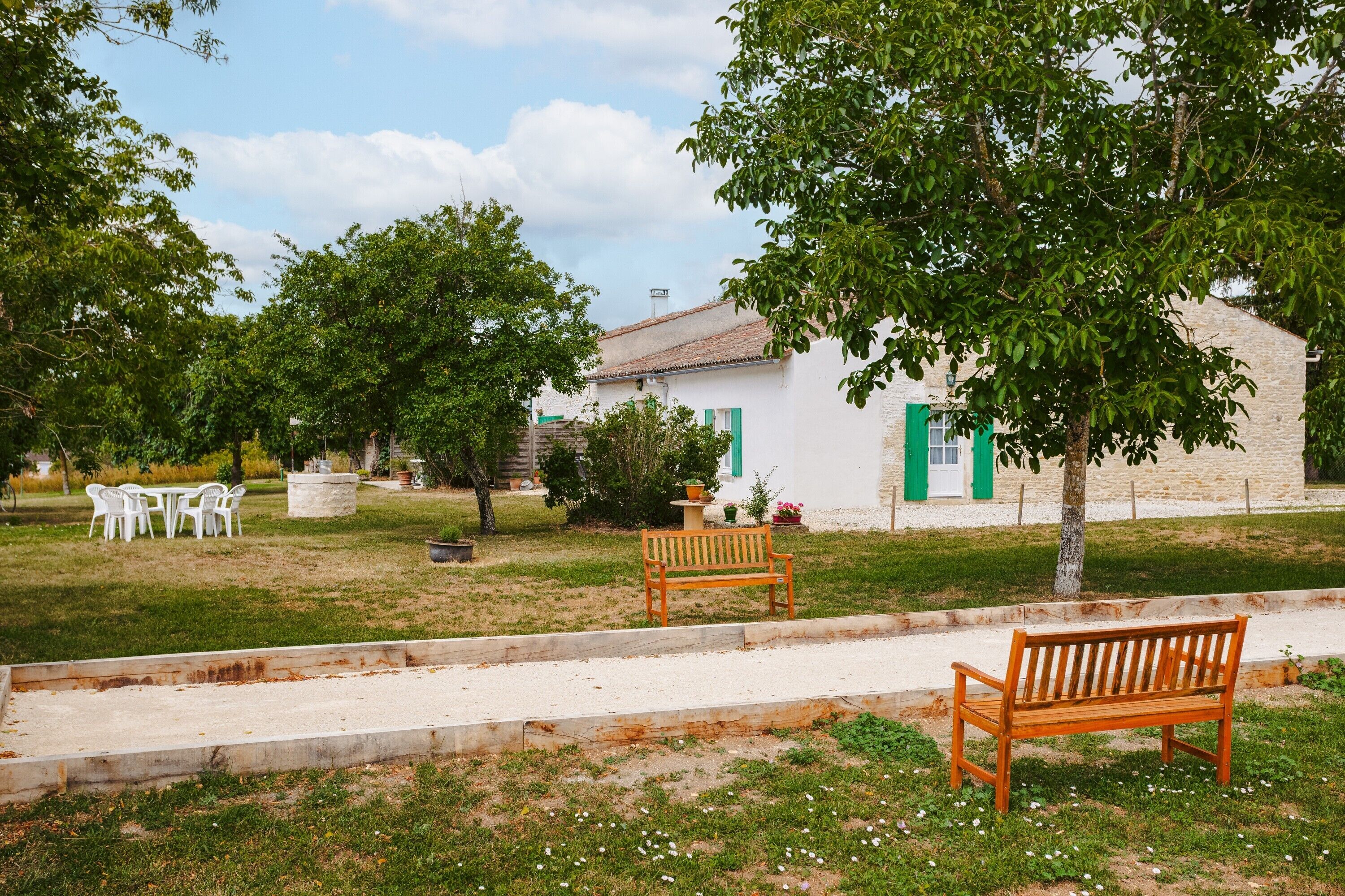 A white building with green shutters, a bench, and a tree in a grassy area.