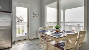 Un coin repas avec une table dressée pour quatre personnes, un réfrigérateur et une vue sur l’océan grâce à de grandes fenêtres.