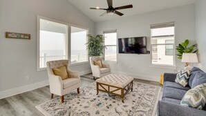 Un salon spacieux doté d’une grande fenêtre, d’un ventilateur de plafond, d’un téléviseur à écran plat et d’une plante décorative.