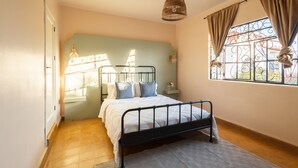Un dormitorio con cama, ventana con cortinas, lámpara colgante y vista al exterior.