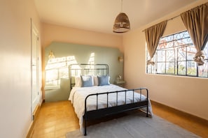 A bedroom with a bed, a window with curtains, a hanging light fixture, and a view of the outside.