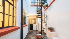 Un estrecho callejón con suelo de baldosas, una escalera de metal negro y macetas con plantas.