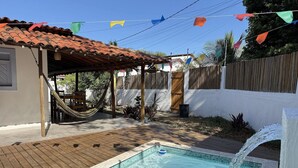 A backyard with a swimming pool, wooden deck, and a hammock. - Oceana Suites Vila Cajarana (Tibau do Sul)
