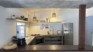 A compact kitchen with a built-in gas stove, stainless steel refrigerator, and hanging utensils. - Oceana Suites Vila Cajarana (Tibau do Sul)