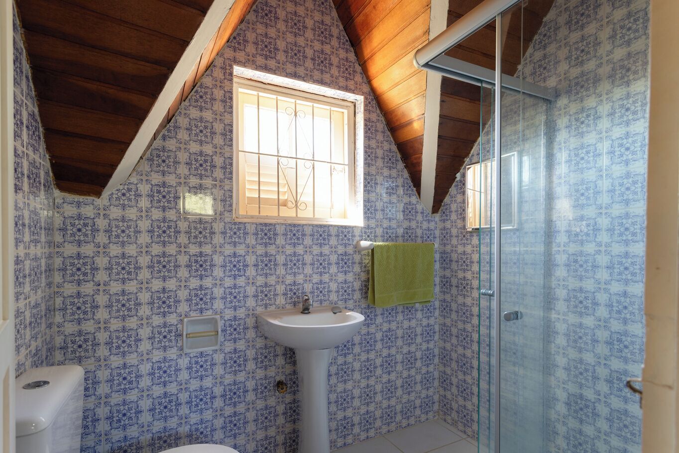 A bathroom with blue patterned tiles, a white sink, a window with bars, and a glass shower door.