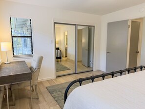 Une chambre à coucher comprenant un lit, un bureau, une chaise, une fenêtre avec des stores, une porte coulissante et une porte.