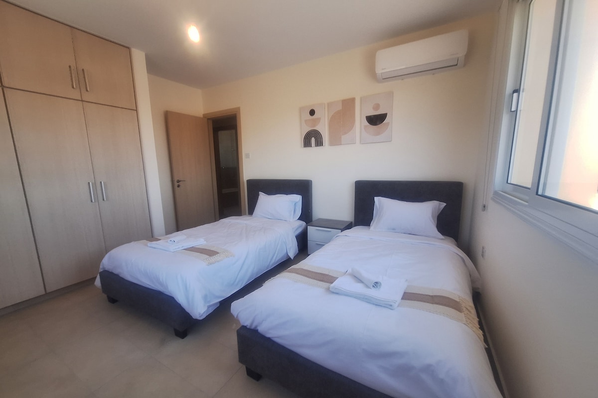 A hotel room with two beds, a wardrobe, and an air conditioning unit.