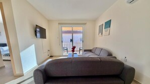 Una sala de estar moderna con un sofá grande, un televisor de pantalla plana montado en la pared y un puerta corrediza de vidrio que da a un balcón.