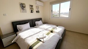Un dormitorio con dos camas, una mesita de noche y un ventanal con vistas a la ciudad.