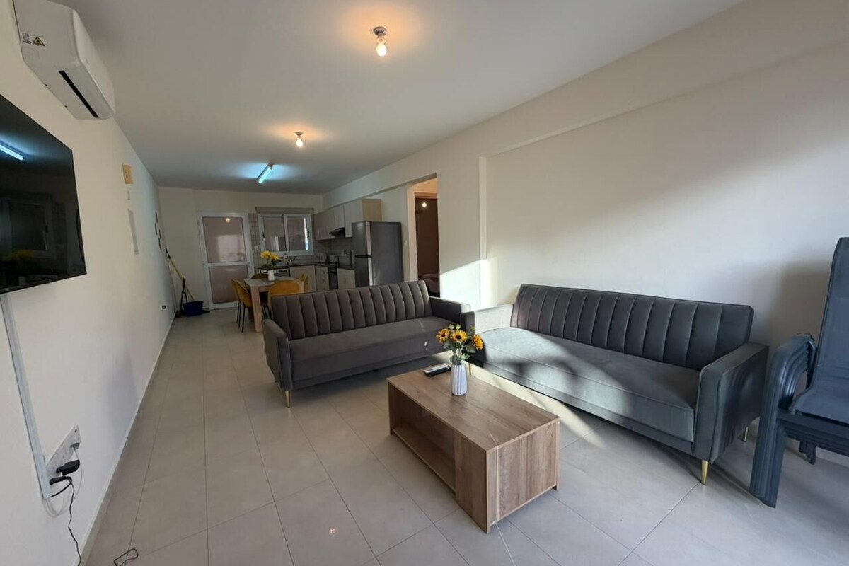 A modern living room with a grey sofa, a wooden coffee table, and a TV mounted on the wall.