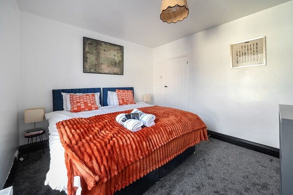Una habitación de hotel con una cama, una mesita de noche, una lámpara, un cuadro enmarcado y una puerta.
