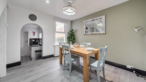Une cuisine moderne dotée d’un four encastré et d’un coin repas avec une table en bois et des chaises blanches.
