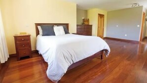 A bedroom with a wooden floor, a bed with white bedding, a nightstand, and a dresser. - Delightful 4-bedroom house in peaceful Connemara Countryside (Moycullen Galway)