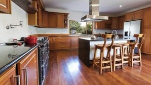 A modern kitchen with wooden cabinets, a central island with chairs, and a stainless steel range hood. - Delightful 4-bedroom house in peaceful Connemara Countryside (Moycullen Galway)
