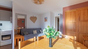 A dining area with a wooden table, a vase with flowers, a grey sofa, and a kitchen in the background.