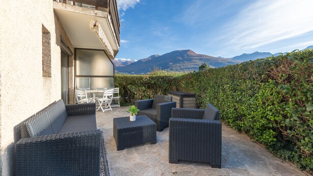 An outdoor patio with wicker furniture, a table, and chairs, overlooking a mountainous landscape.