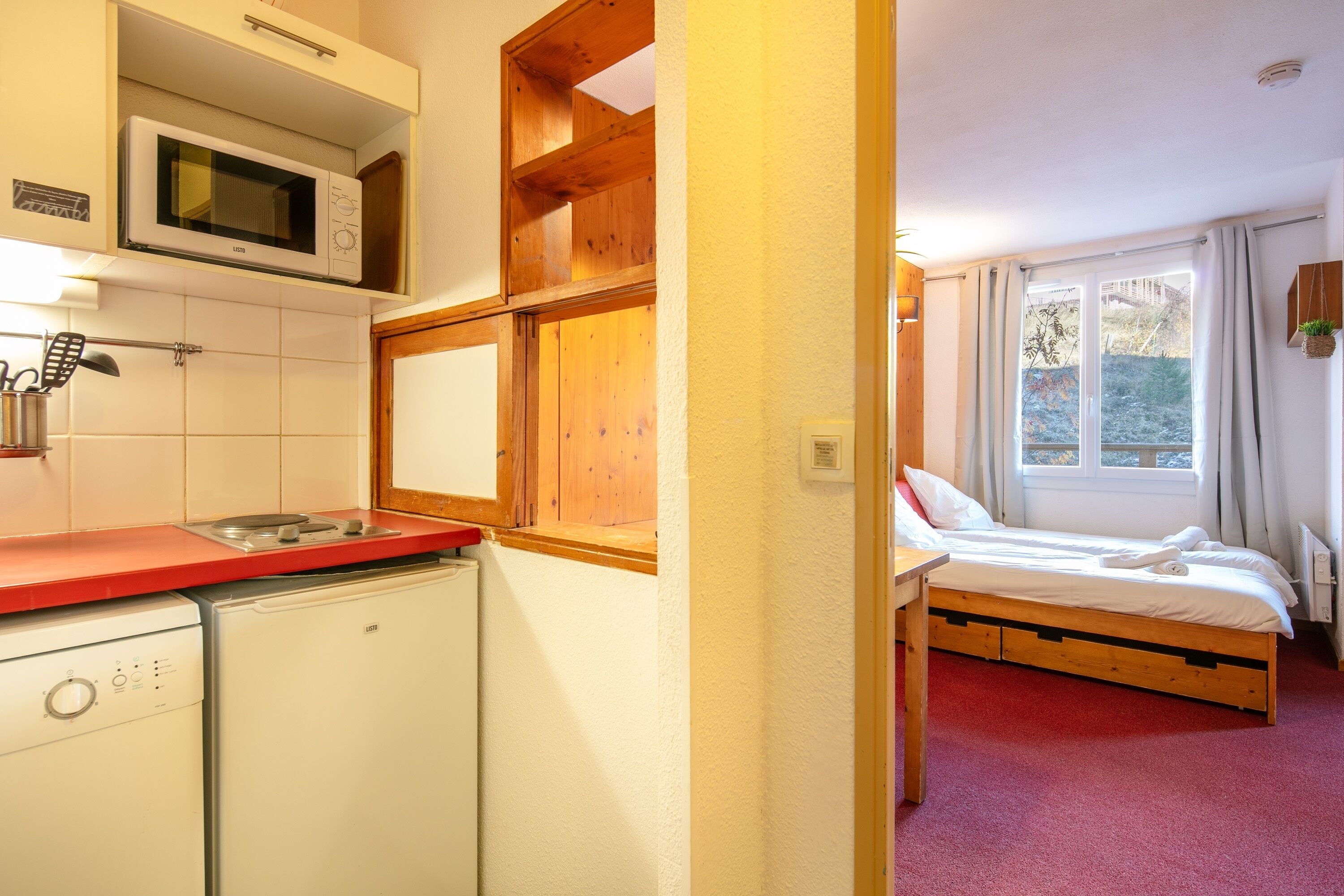 Habitació compacta amb llit, microones, nevera petita i prestatge de fusta.