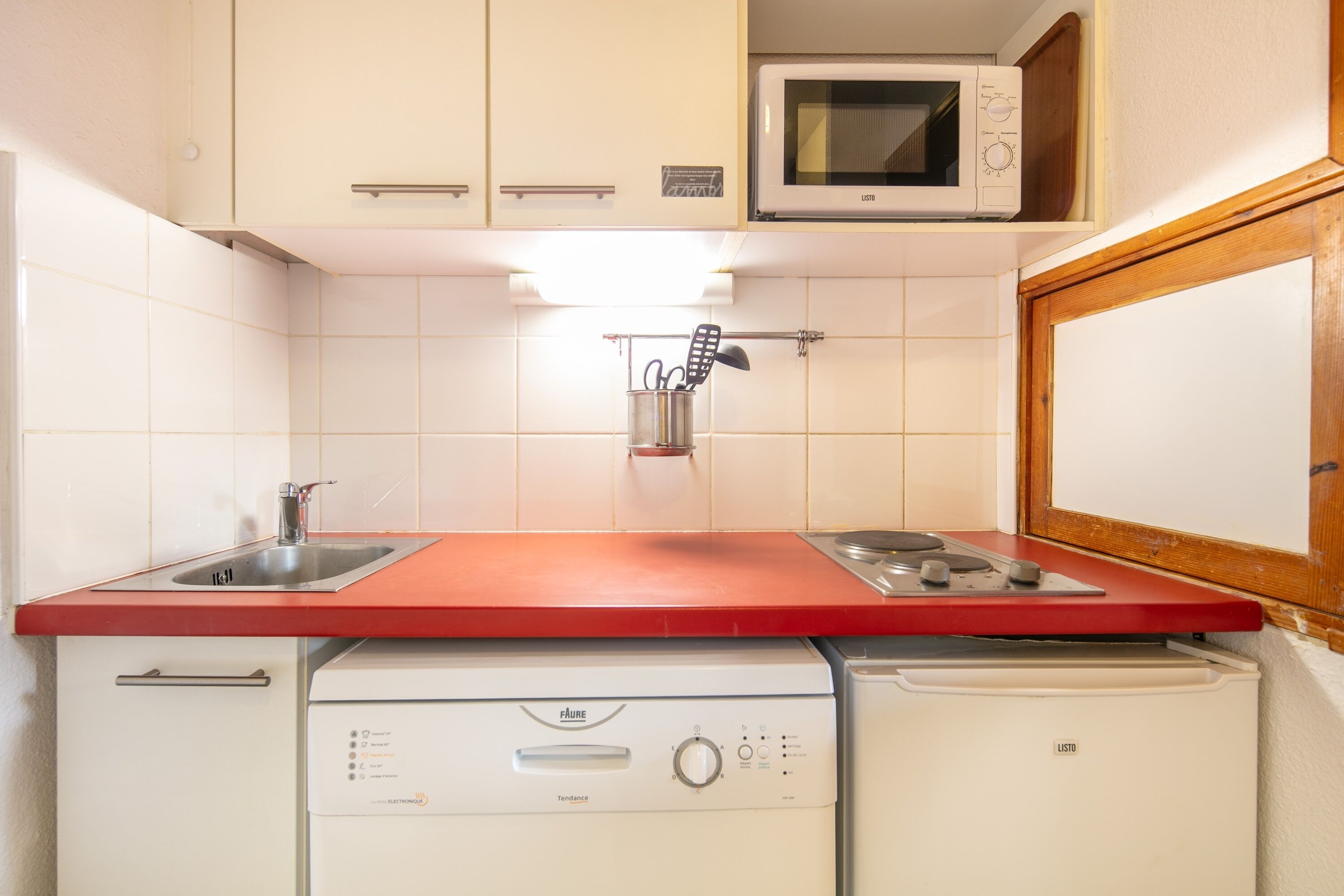 A compact kitchen with a red countertop, a built-in microwave, a dishwasher, and a stove.