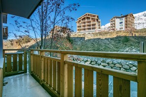 A wooden balcony with a stone wall, overlooking a mountainous landscape with buildings. - Les Bergers - Proche Station de Ski (Huez)