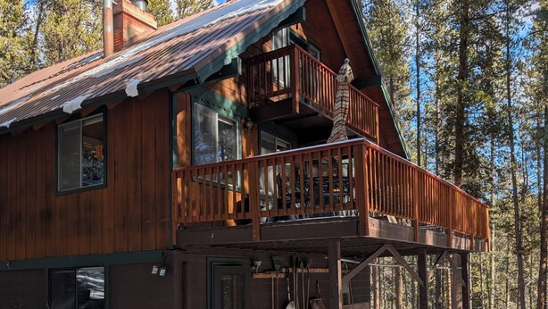 Une cabane en bois dotée d’un balcon, entourée de neige et d’arbres.