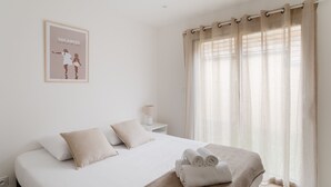 A bedroom with a bed, pillows, a bedside table with a lamp, and a window with curtains. - Couleur Sable - 1km de la Plage (Dinard)