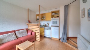 Ein kompakter Wohnbereich mit Küchenzeile, einem roten Sofa und einem kleinen Holztisch.