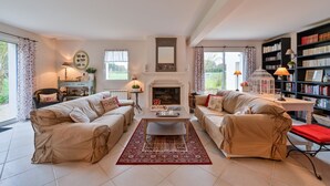 Un salón con dos sofás color beige, una mesa de centro, una chimenea, una estantería y una ventana con cortinas.