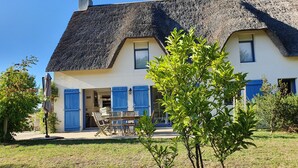 Una casa con techo de paja, contraventanas azules y un pequeño jardín.