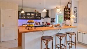 Una cocina con una isla de madera, taburetes de bar, lámparas colgantes y una variedad de utensilios de cocina y adornos.