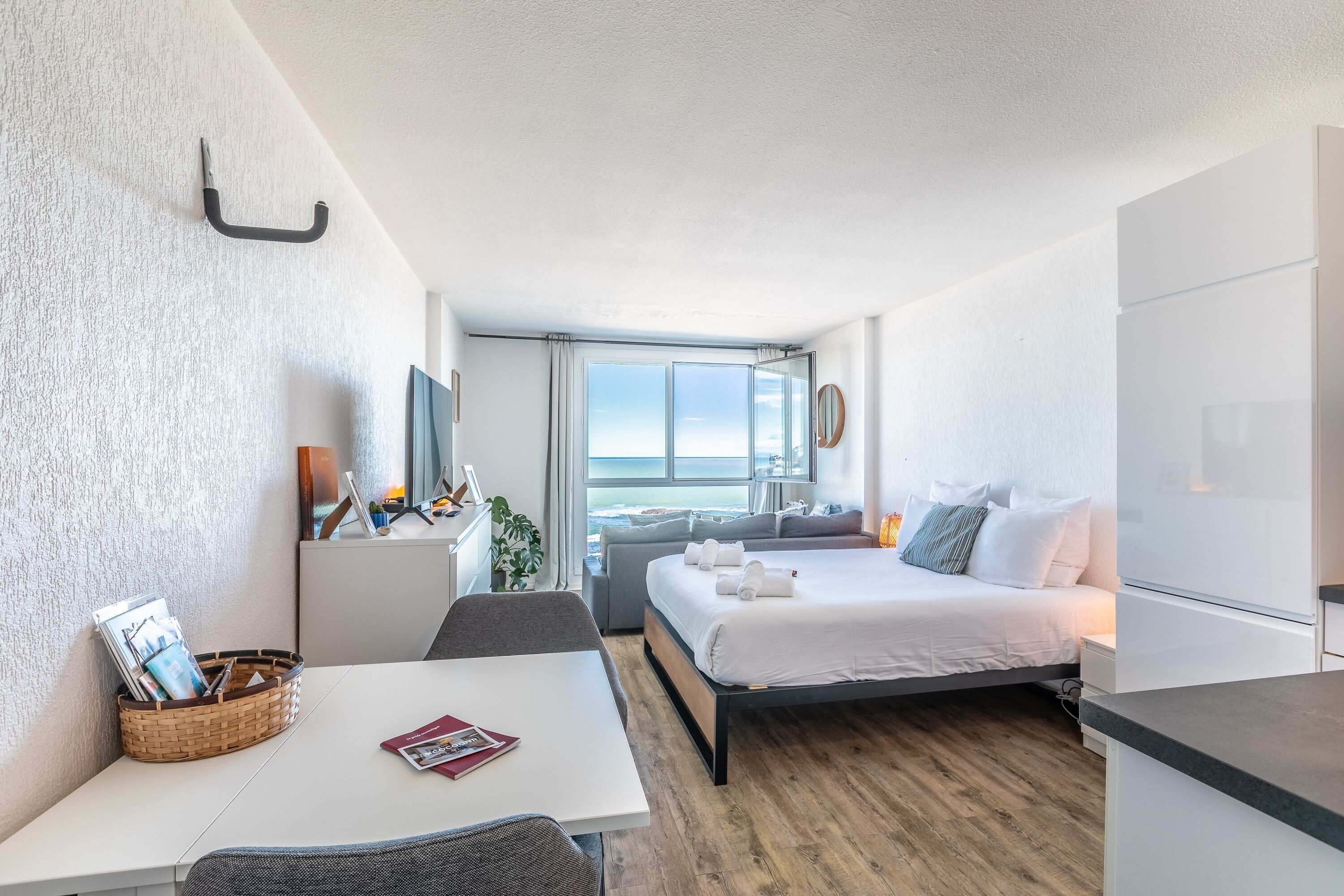 A modern hotel room with a large bed, a desk, and a view of the ocean.