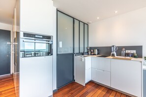 A modern kitchen with a built-in oven, a coffee machine, and a view of the outdoors. - Baïa - Studio vue imprenable sur la mer (Biarritz)