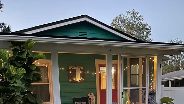 Une maison verte avec un porche, des marches et des guirlandes lumineuses.