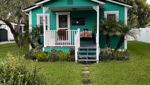 Une petite maison de plain-pied, à l’extérieur vert et aux bordures blanches, dotée d’un porche avec une balustrade blanche et d’un petit marchepied menant à l’entrée.