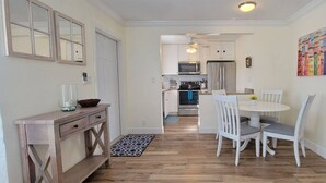 Une cuisine moderne avec des meubles blancs, un coin repas avec des chaises blanches et un tableau coloré au mur.