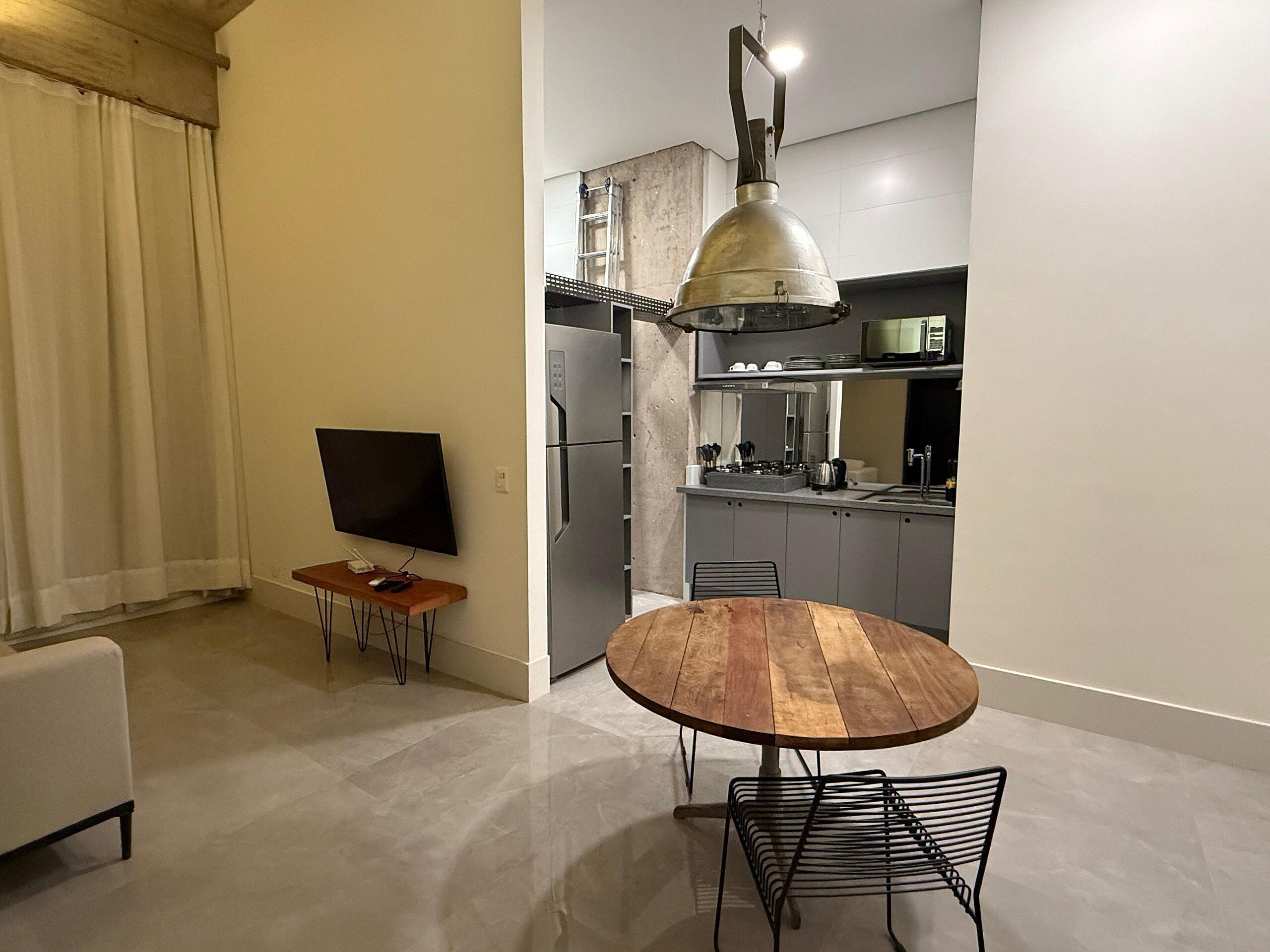 Cozinha moderna com forno embutido, micro-ondas e pia. Há uma mesa redonda de madeira com cadeiras de metal no centro do quarto.