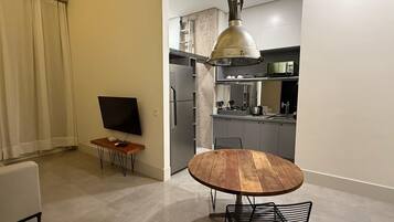 Cozinha moderna com forno embutido, micro-ondas e pia. Há uma mesa redonda de madeira com cadeiras de metal no centro do quarto.