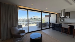 A modern apartment with a large sliding glass door leading to a balcony, a kitchen area, and seating with a view of the cityscape. - Noroeste design comfort and charm (Brasília)
