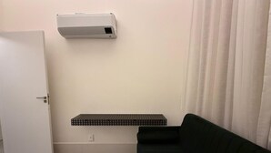 A room with a white door, a black couch, a white air conditioning unit, and a black shelf. - Noroeste design comfort and charm (Brasília)