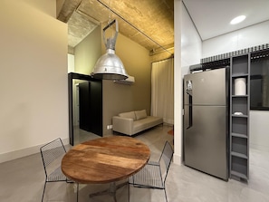 Una cocina compacta con una mesa redonda de madera, dos sillas, un refrigerador empotrado y una lámpara colgante.