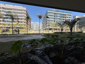 Vista de un moderno complejo de edificios con varios pisos, amplias ventanas y un jardín bien cuidado con diversas plantas y árboles.