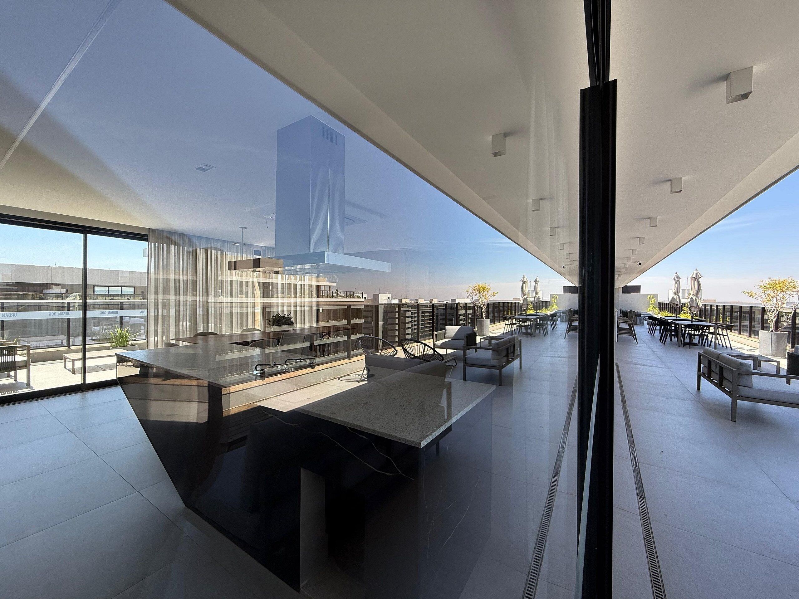 Eine moderne Dachterrasse mit Glasfassade, Außenbestuhlung und Blick auf die Stadtlandschaft.