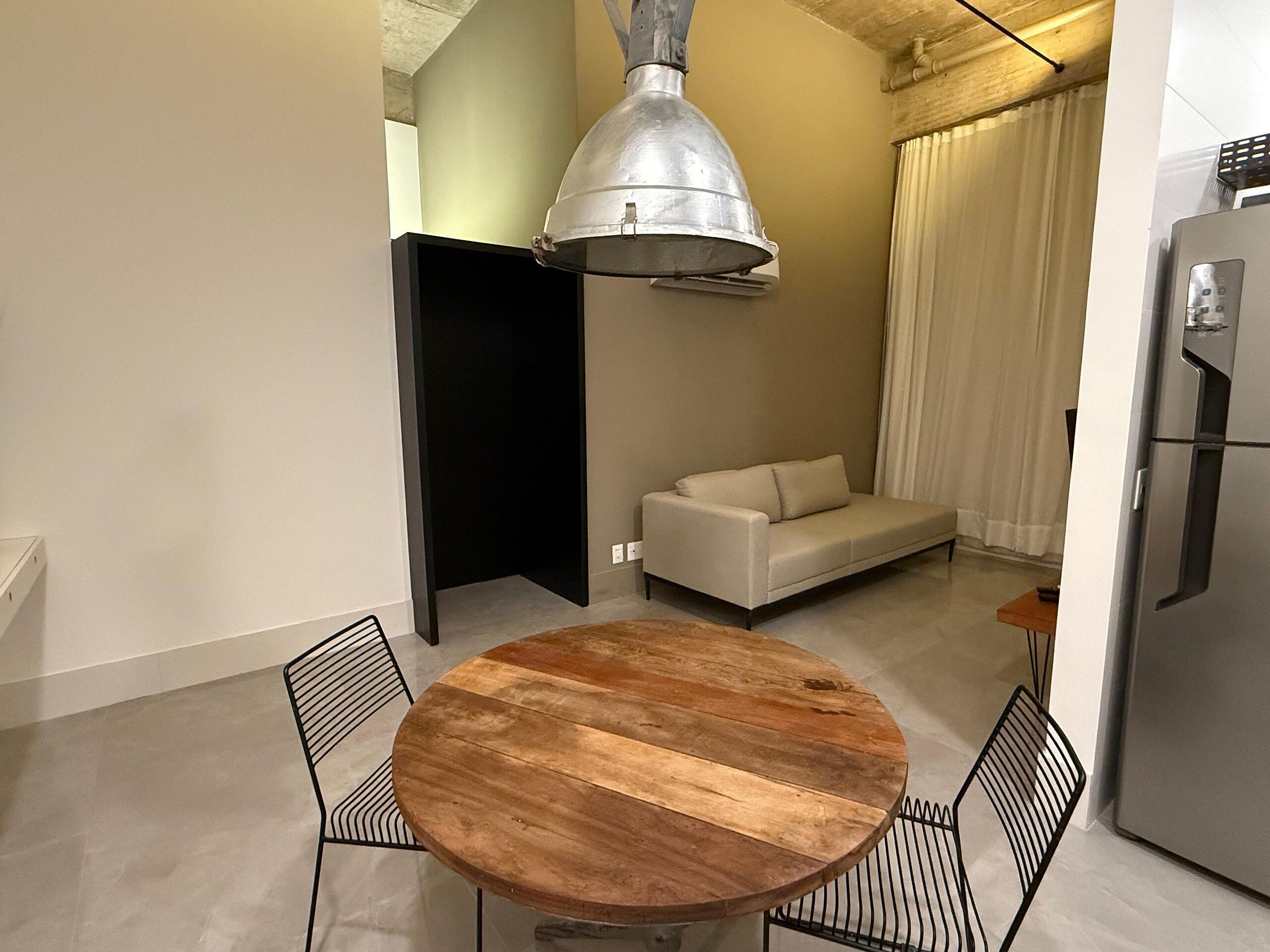 Un espace de vie compact comprenant une table ronde en bois, deux chaises, un canapé et un coin cuisine moderne.
