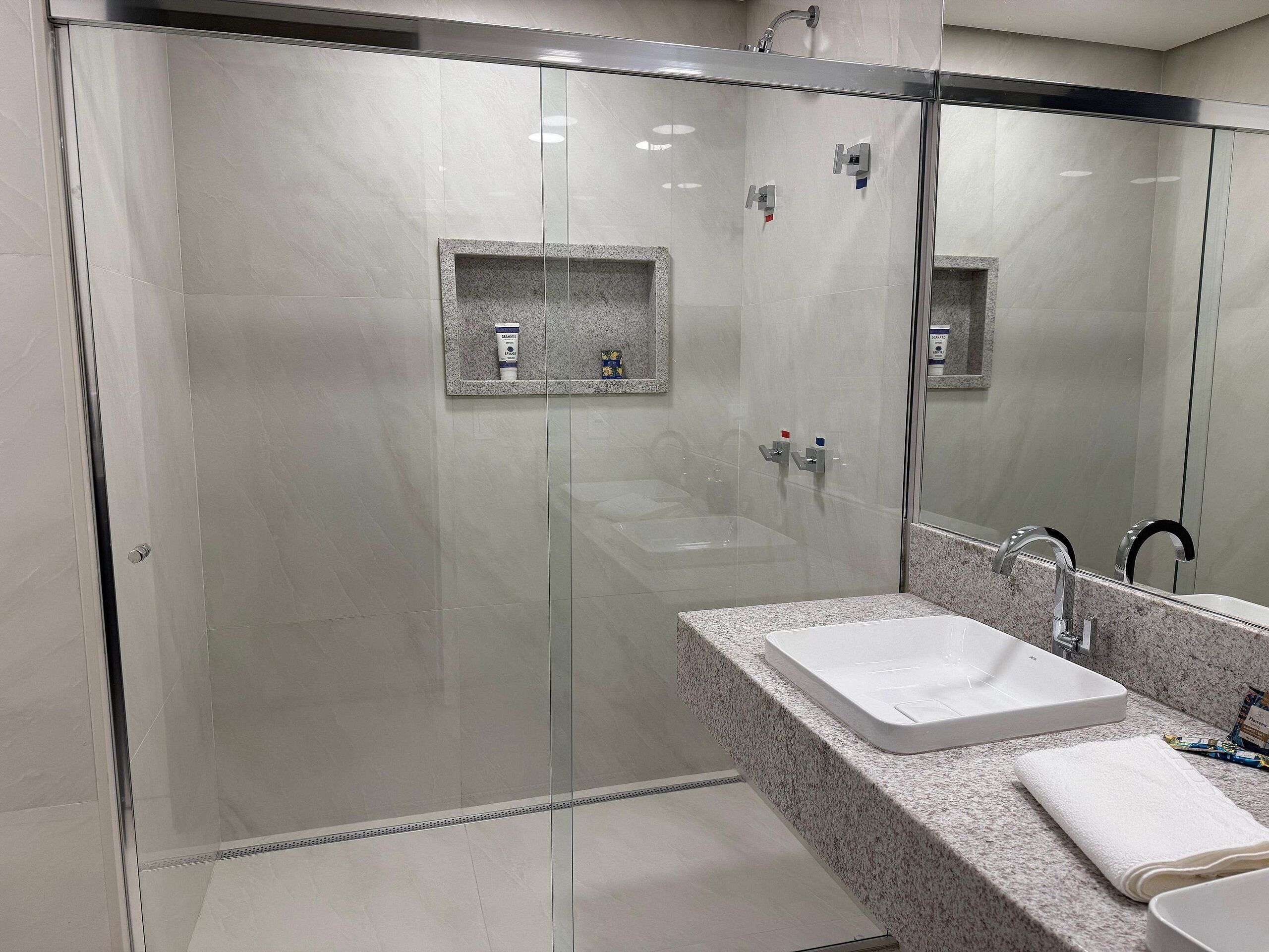 Un baño moderno con ducha envuelta en vidrio, encimera de granito, lavabo blanco y espejo.
