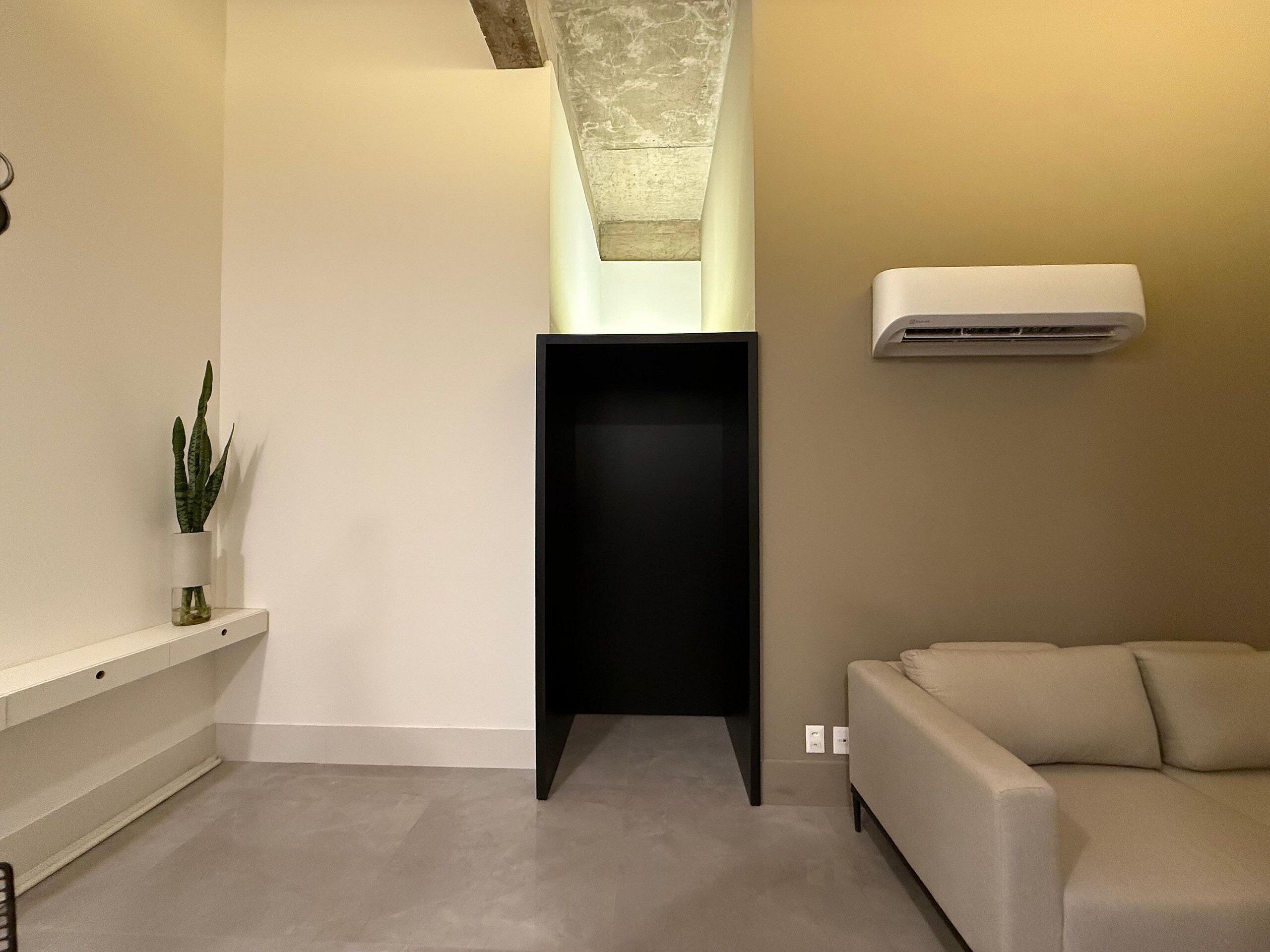A modern living room with a beige sofa, a black cabinet, and a potted plant on a white shelf.