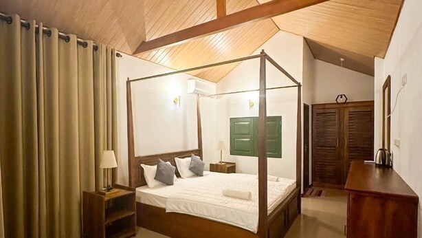 Un lit à baldaquin avec un cadre en bois, une table de chevet avec une lampe et un meuble vert fixé au mur.