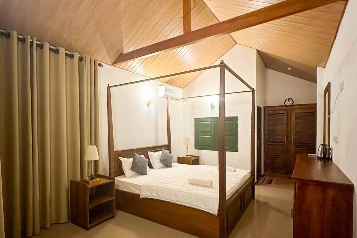A four-poster bed with a wooden frame, a bedside table with a lamp, and a green wall-mounted cabinet.