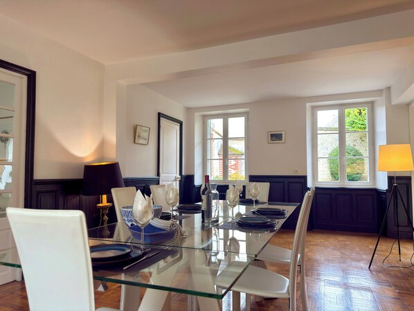 A dining area with a glass table, white chairs, and a lamp.